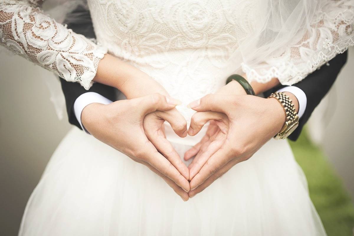 Un couple de mariés forme un cœur avec leurs mains, symbolisant l'amour et l'unité, pour illustrer la validation du mariage à l'étranger