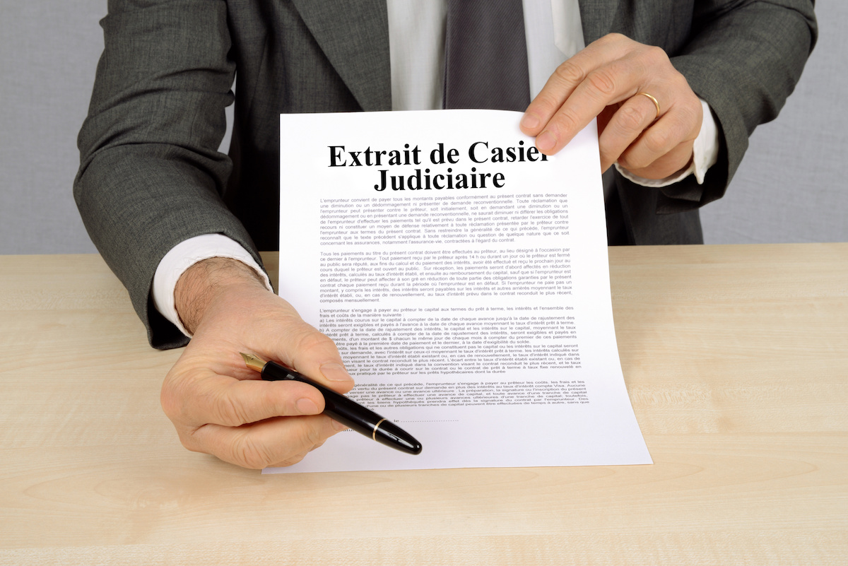 Personne en costume présentant une feuille intitulée Extrait de Casier Judiciaire et tenant un stylo