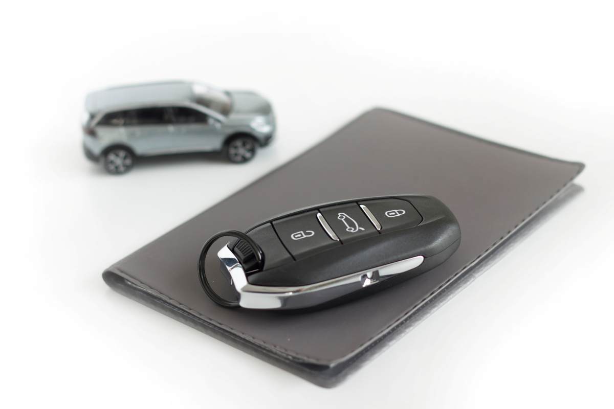 Clé de voiture posée sur un étui gris, avec une voiture miniature en arrière-plan