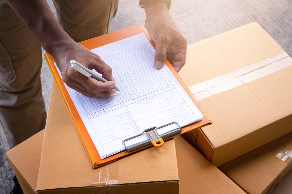 Personne remplissant une fiche sur un porte-documents posé sur des cartons