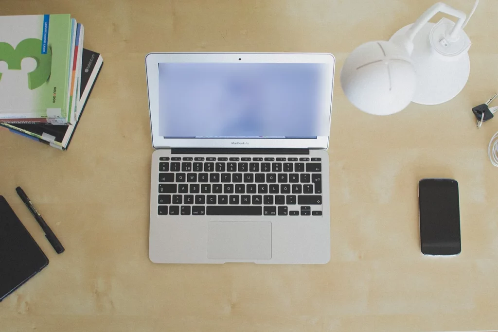 Ordinateur portable, téléphone et carnets sur un bureau en bois vu du dessus